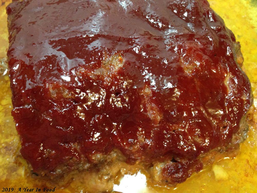 meatloaf in a greasy pan with ketchup sauce over top, the standard