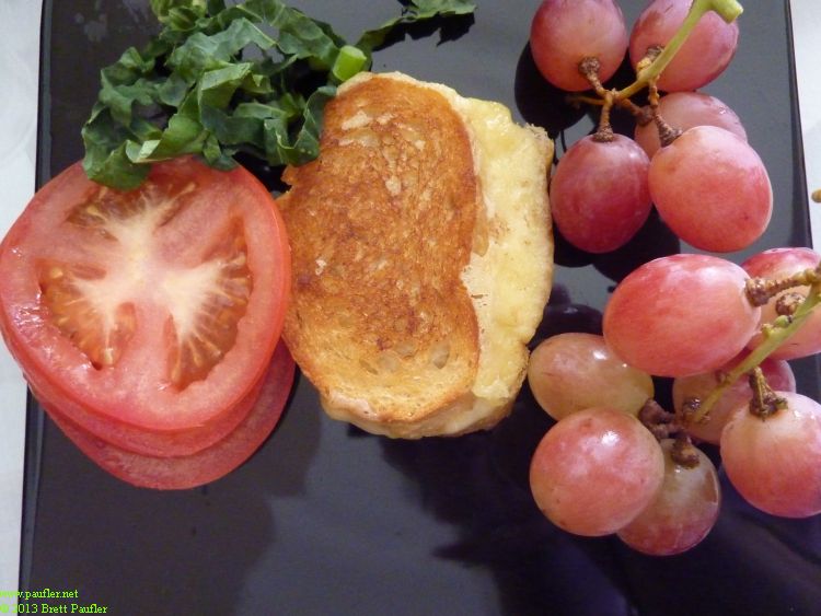 Grilled cheese decoratively presented on a black plate with slices of tomato and grapes