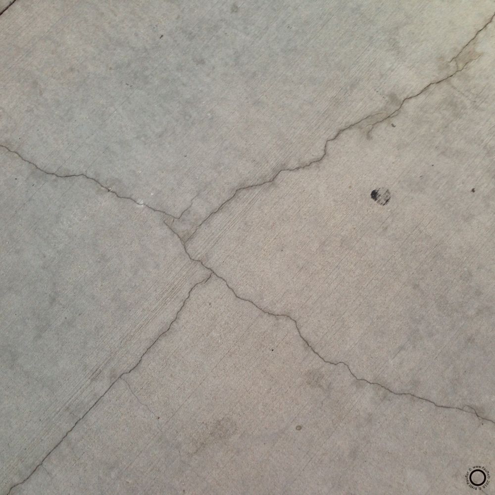 Cracks in the sidewalk, splitting the image into four diagonalish pieces, with some odd bit of concrete staining here and there
