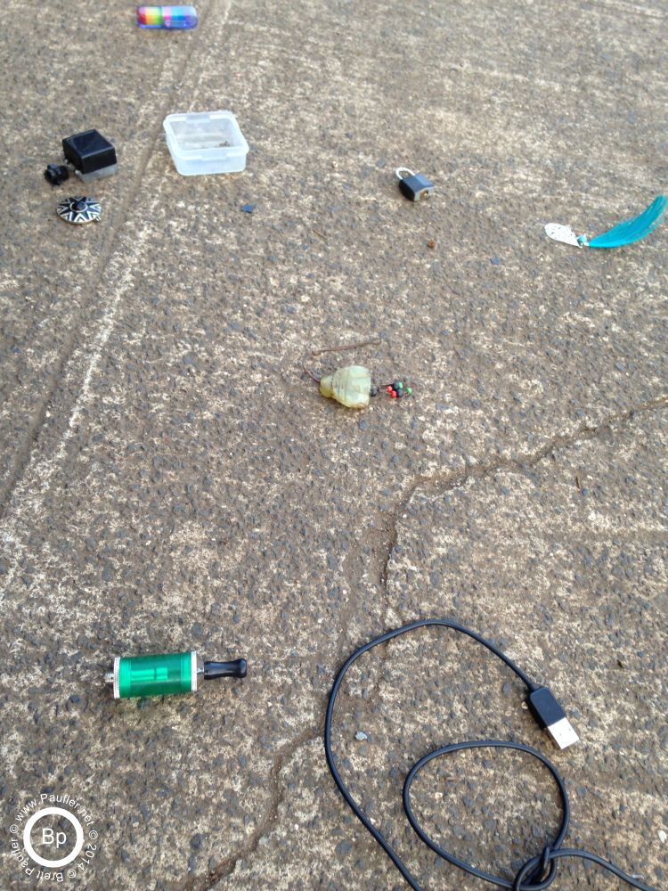 Odds and ends on the sidewalk. Lock, feather earring, computer cable, a pipe, perhaps will residue...