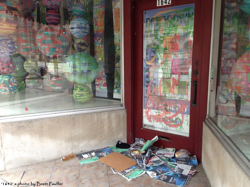 a store shop, the windows papered over, paper lanterns as the shop display, numerous free papers and a little personal detritus, strewn around the door, this shop does not look like it is open for business to me