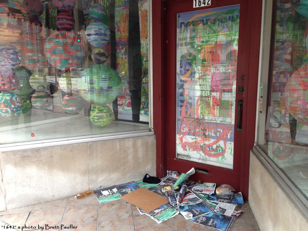 1642 a store shop, the windows papered over, paper lanterns as the shop display, numerous free papers and a little personal detritus, strewn around the door, this shop does not look like it is open for business to me