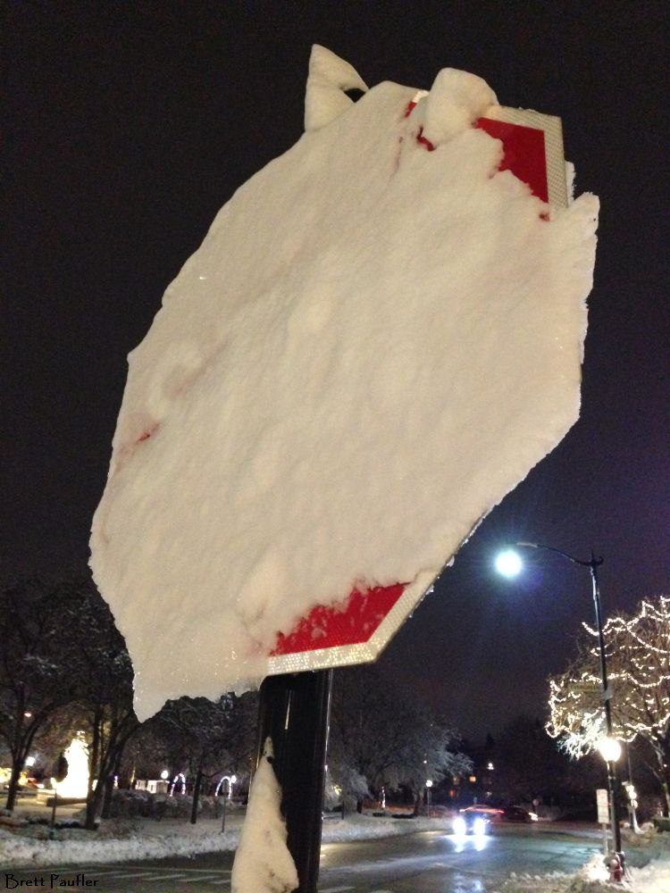 Stop! A stop sign covered in snow, but it is not all that bad, as the streets are clear, verified by the car driving by