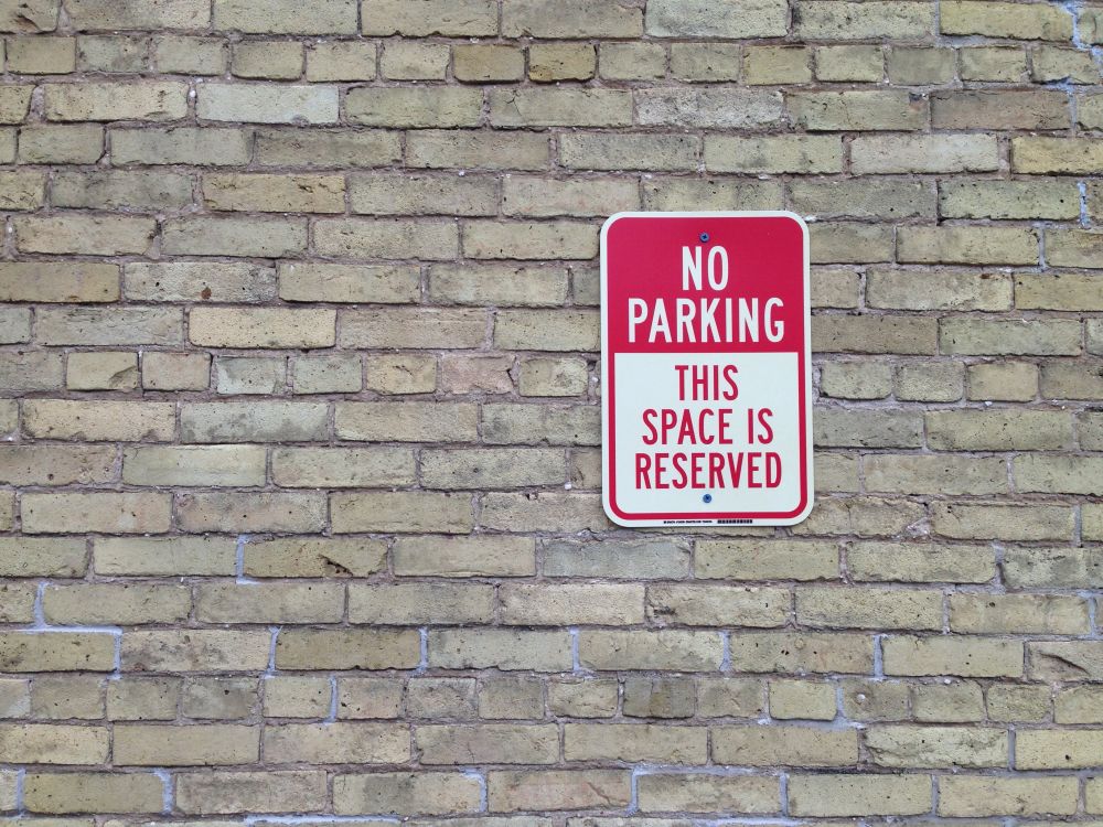a No Parking sign attached to a grey brick wall, the image is more about the grey bricks, pleasing to look at, than the sign, as the sign is totally out of context, even if it is the sign that calls to the text, below