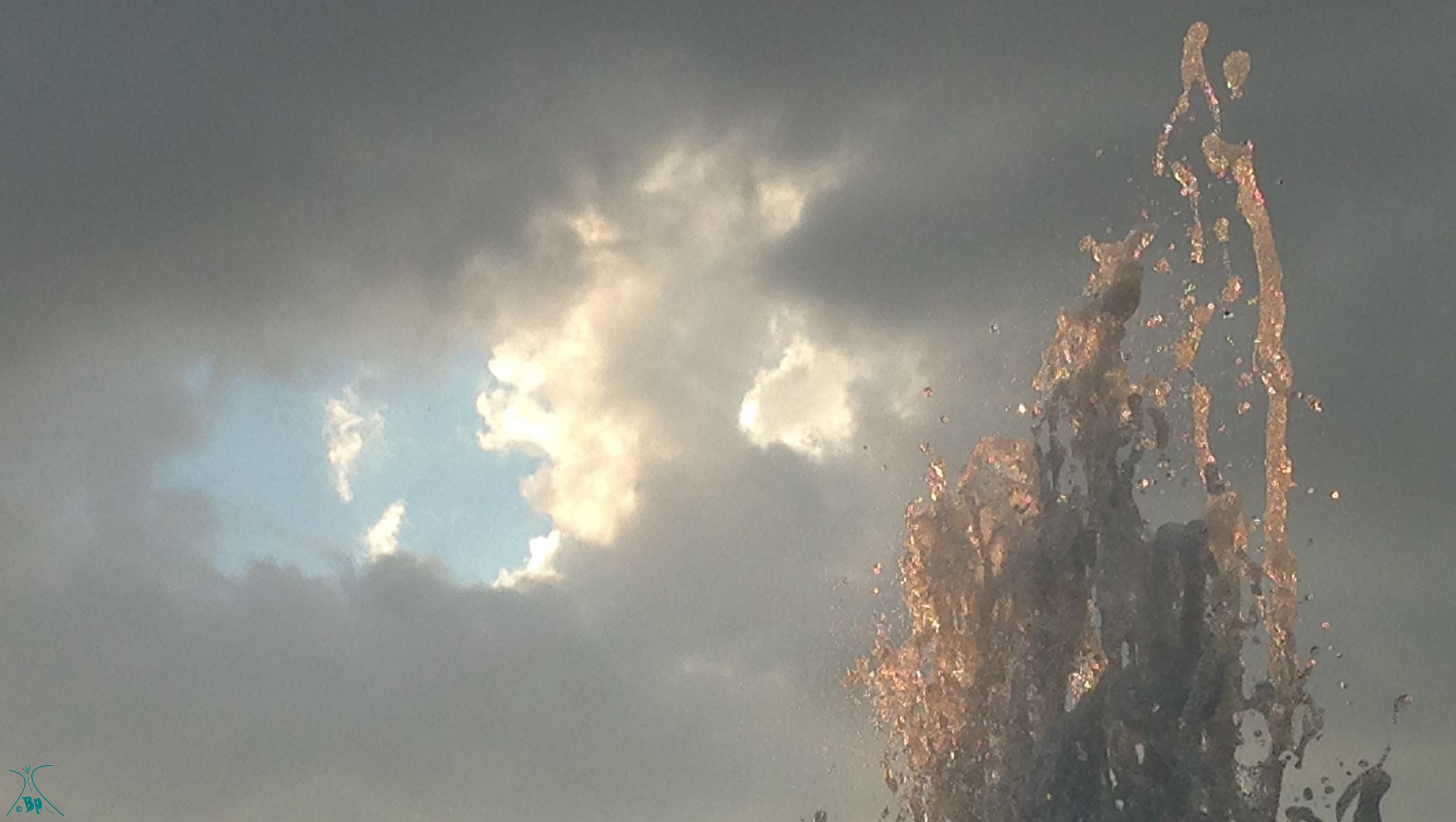 The top of a waterfountain juxtaposed with the clouds beyond, I like the way the light hits the water