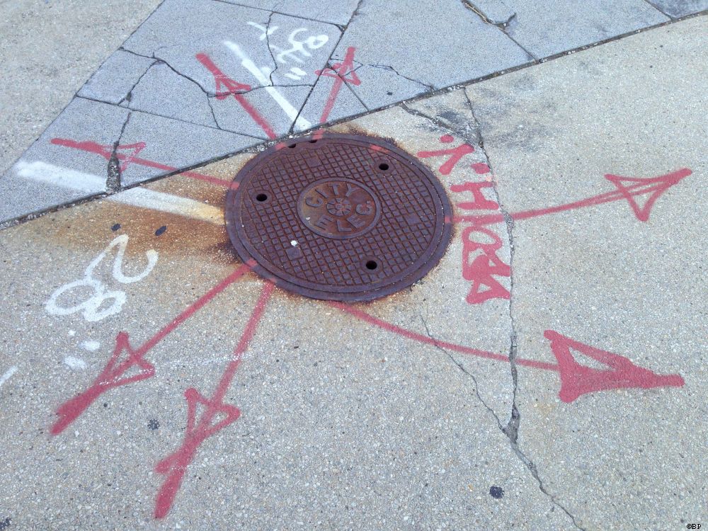 Red construction markers spray painted around a manhole, showing arrows going in a variety, call it seven, different directions, arrows being the theme of these two images