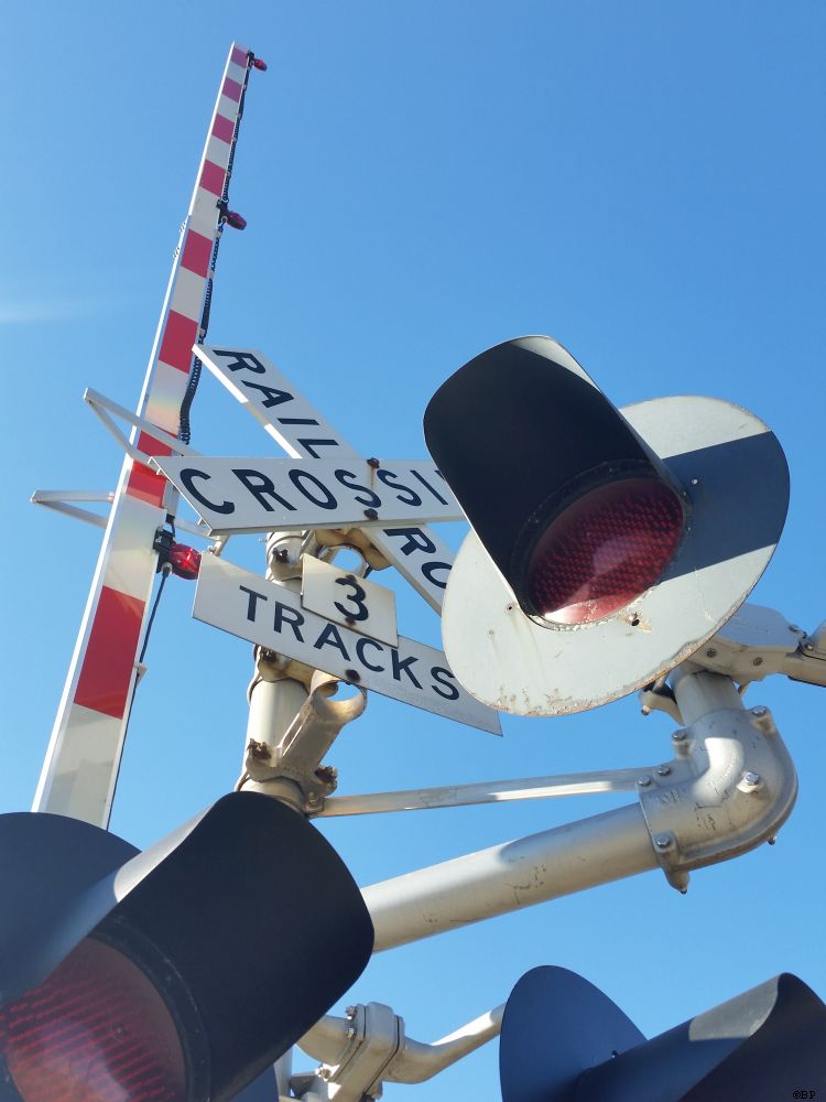 Fully illuminated railroad crossing street arm, that thing that goes down and prevents cars and pedestrians from entering the intersection and crossing the tracks, crossing guards, likely, nice blue sky