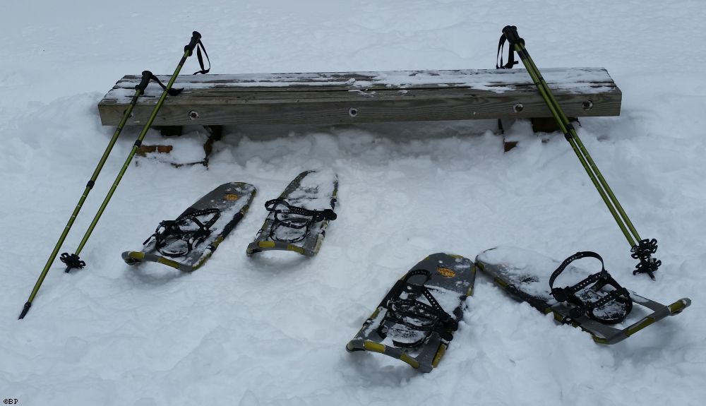 Two sets of snowshoeing gear lying next to a bench, poles, and snowshoes, it was an interesting walk, though, the snow wasn't that deep, and walking where another had already stepped might have been technically easier, still, a fun experience, says the man, months later, sweating from the summer heat