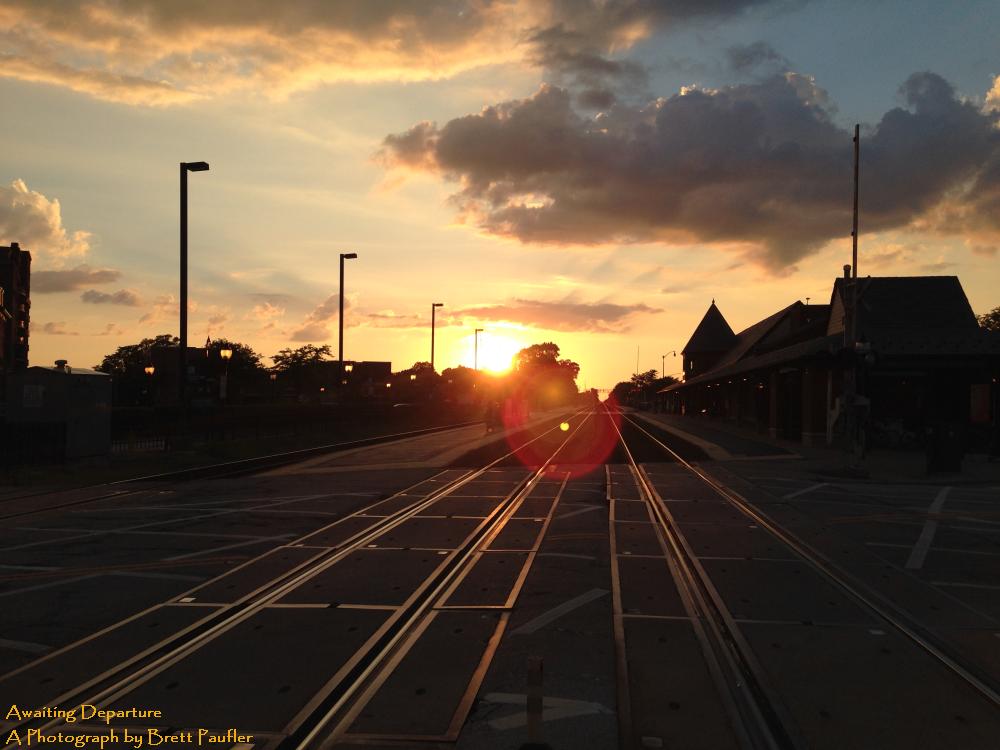 looking down train tracks into the sunset, I especially like the lens flare at the center, the clouds in the sky, and the amber light reflected off the tracks, while the station itself stands in silhouette to the right