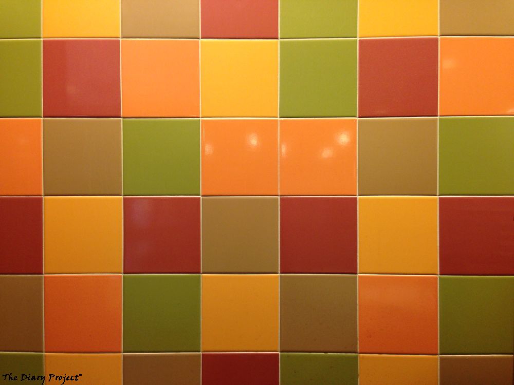 Tile pattern on the wall, which seems like a good of picture as any about the place, I enjoyed sitting there, and it was a solid sandwhich, but not inspired, this is an image of red orange, yellow, and green tiles, with the reflection from some overhead lights shining through