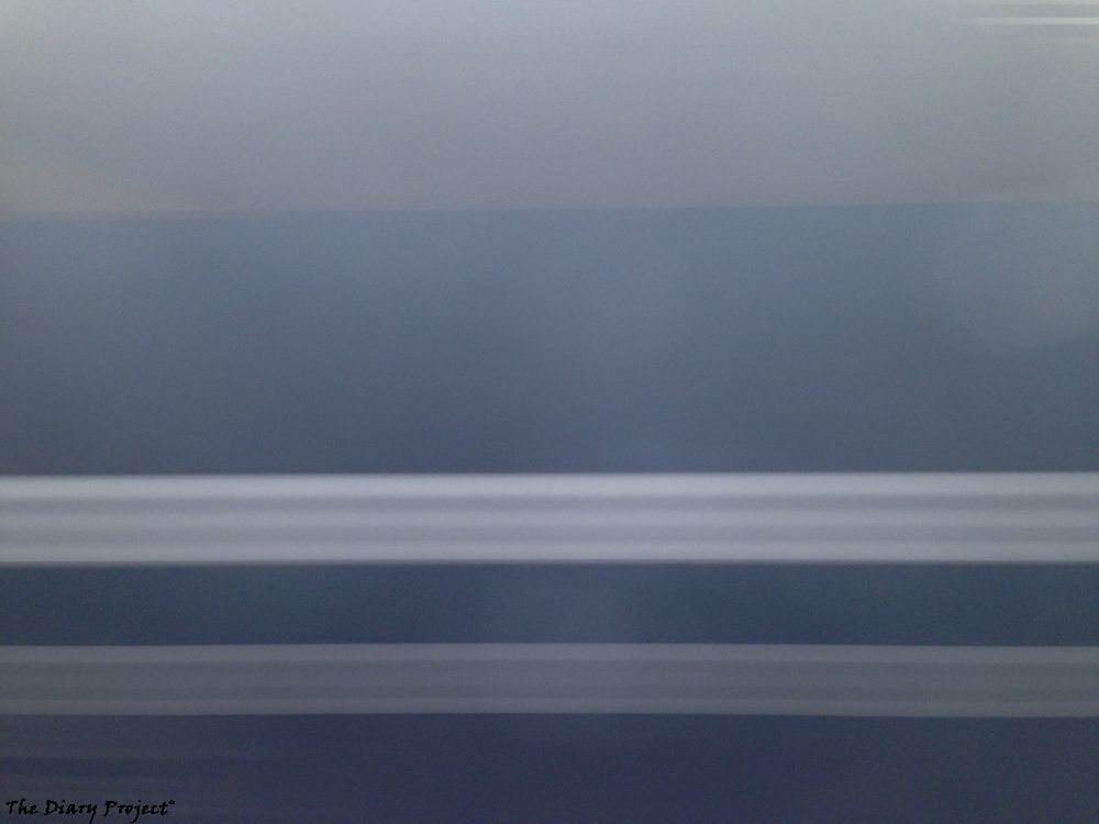 side of a commuter rail car, blurred as it or we go by, streaks of blue and grey