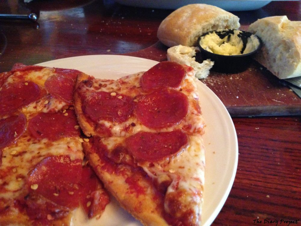 Pizza on a plate with bread and butter in the background, this is good pizza, corn meal thin crust, very good, loaded with cheese and pepperoni, all for the unbelievable price of ten bucks, with purchase of drink