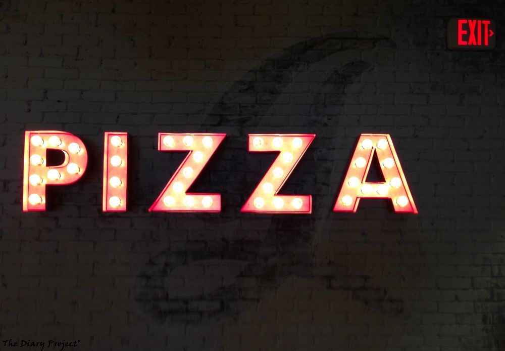 A nice little sign with incandescent bulbs that reads pizza, with an exit sign in upper right, the real question is what the faded paint in the background is supposed to mean or indicate or merely what was there before