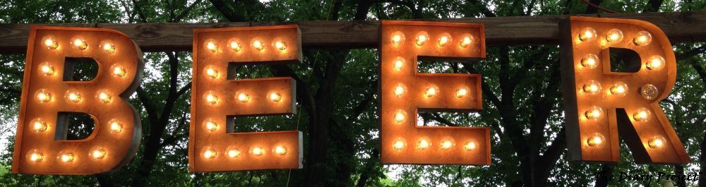 A Beer sign with tree leaves in the background, nothing more, nothing less