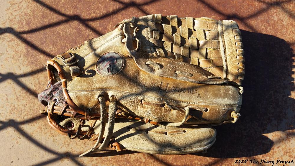 A Baseball Glove in the shadow of a chain link fence