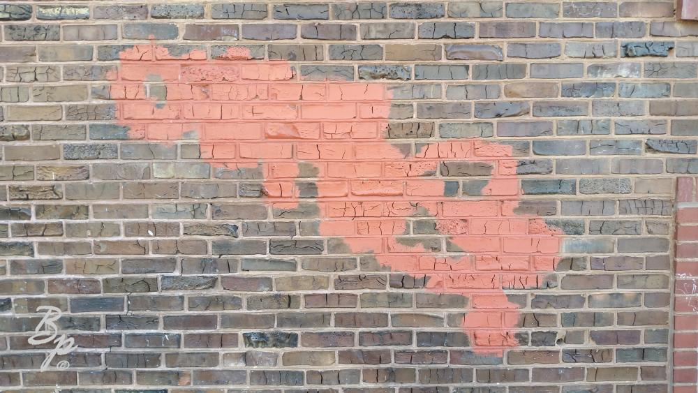 An old brick wall, brownish bricks with a very small area of red brick infill, the focus of the picture being a large red splotch of red paint