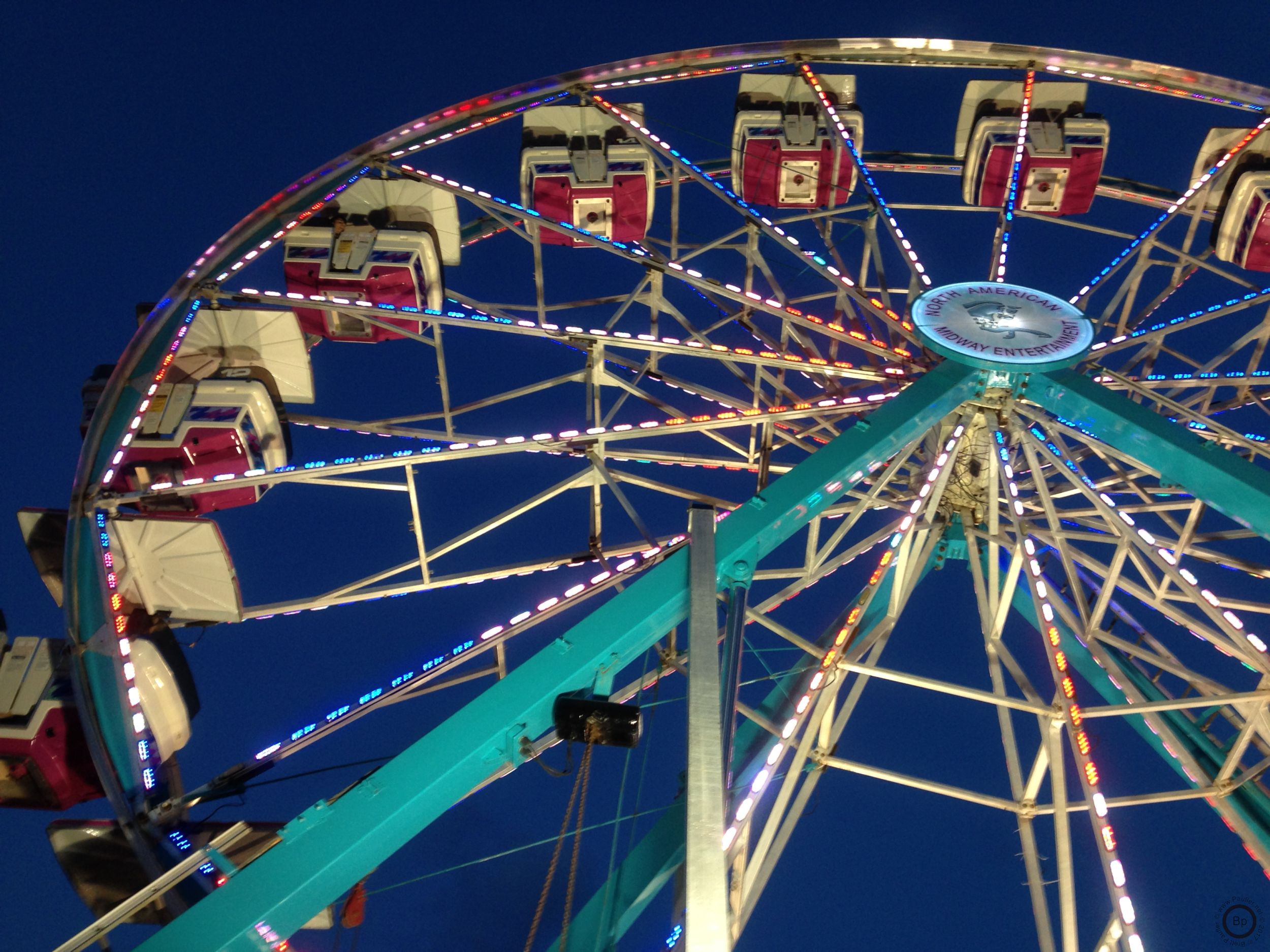 What we have here is a caged Ferris Wheel, so family seating, it is a nice enough image, looking from the bottom to the top, the next day on social media or in the paper or maybe some brochure at the carny, I came across more or less the same shot, so a classic, everyone should have one, everyone should take one, not shown are the musical productions, not as easy to photograph, to get the feel, maybe I need to work on that, the crowd feel, without utilizing faces, I guess that is part of the problem, anyhow, a ferris wheel, concert stage to the right, left unshown