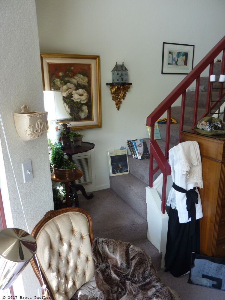 This is an old loft apartment I used to have in Walnut Creek and the Sequence of events and or images is what I sent to my mother on mothers day, this is an establishing shot of the stairway, leading up to the second level, the item of interest is the small house on a pedestal, call it art, scattered about are the library books I was reading att the time, chair, fur, reading place basically, lamp, plenty of light from the two story windows... that is a vacumn cleaner dressed as a maid, and the desk next to it had a wonderful story, it came with a fake diamond ring and a semi will, so from an estate, with notes and history, Doctor Something Dresser, it was haunted, in a good way