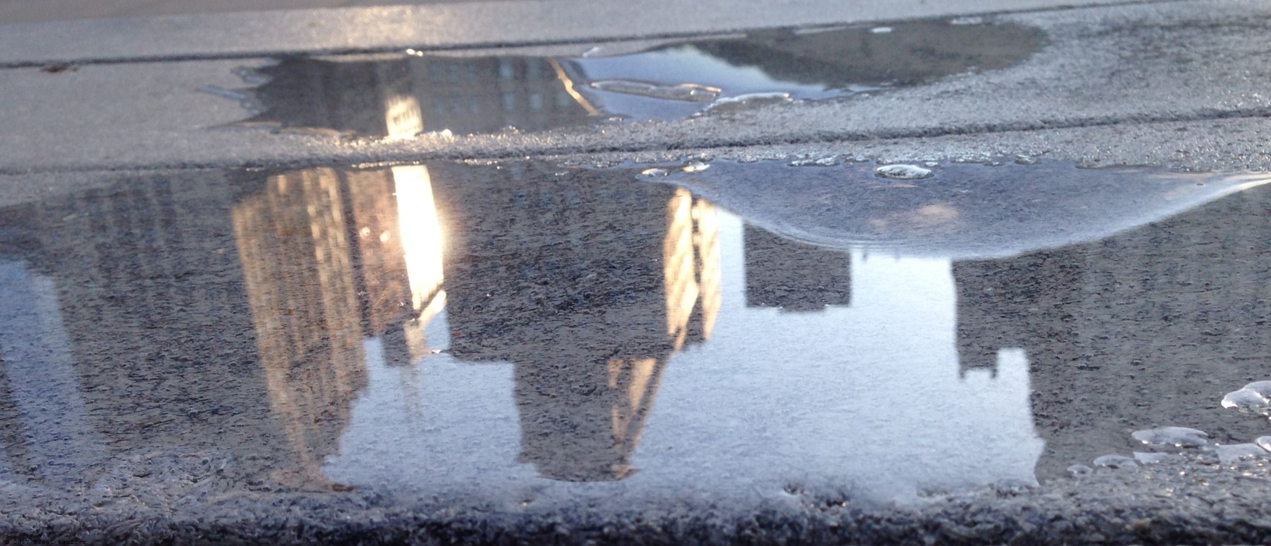 Cityscape reflected in an puddle of water on a picnic table, this image, with the buildings right side up, is actually the reversed one, all other images on the page are the same as this one or its reverse, I cannot be bothered to write in all the possible transform combinations, so if it is not reversed, well, it should be, update your browser, bro