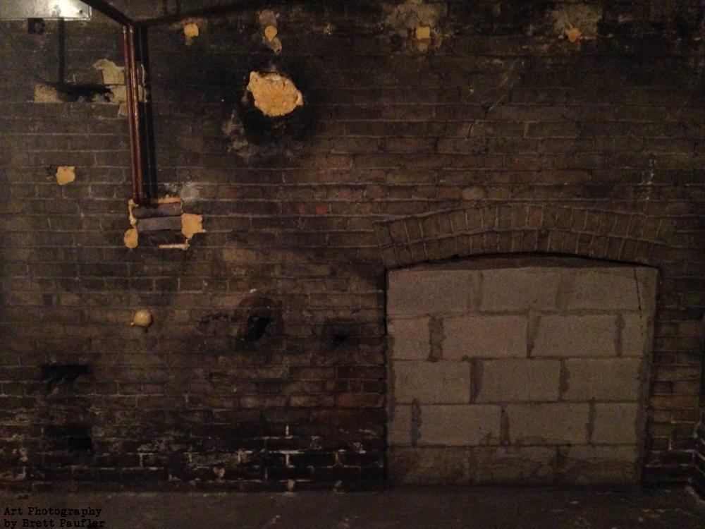 we are just looking at the wall of a brick basement, century old construction, closed in brick archways, wires, splotches patched up