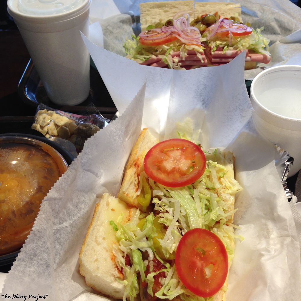 A table set for two complete with two sandwiches, plastic bowl of can opened chili, styrofoam cups for water, and delightfully convect plastic trays