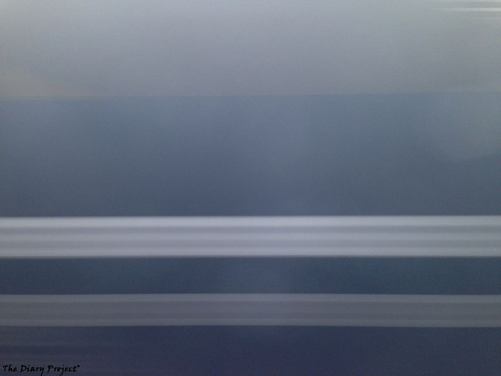 side of a commuter rail car, blurred as it or we go by, streaks of blue and grey