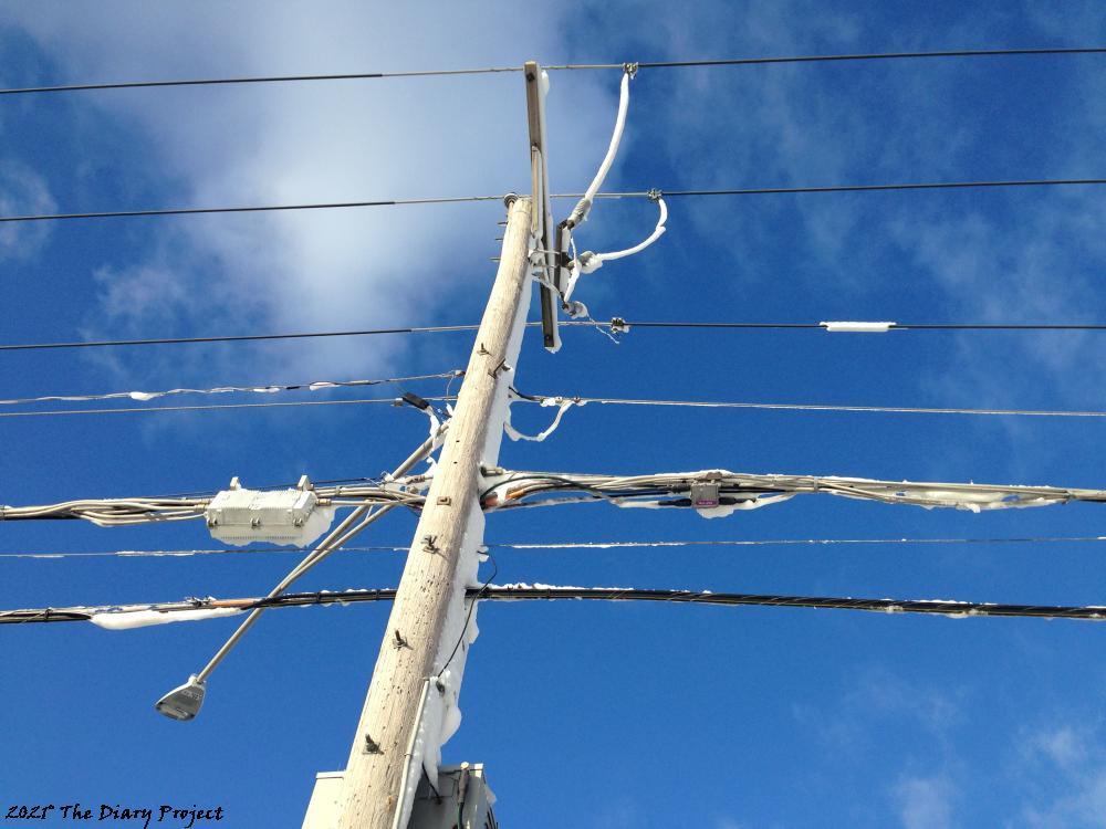 Back in November of 2018 there was a massive snowfall accompanied by horizontal wind which cause snow to stick to the sides of buildings and down dozens upon dozens of power lines.  The image itself is of a power pole complete with power lines covered in snow (originally an inch or two thick) a day or two later (so, now a circular casing of ice has mostly fallen off) as the sun shines brilliantly, giving the sky a wonderfully saturated blue hue.